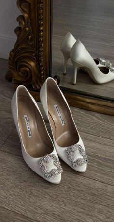 a pair of white high heeled shoes sitting on top of a wooden floor next to a mirror