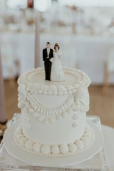 a white wedding cake with a bride and groom figurine on the top tier