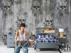 a young man holding a skateboard in front of a wall with skulls on it