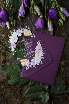 wedding stationery with flowers and greenery laid out on a wooden table next to purple envelopes