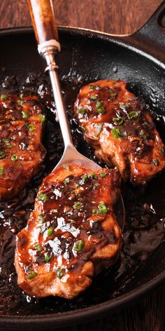 two pork chops being cooked in a skillet with brown sauce and green onions