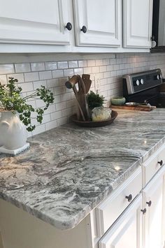 a kitchen with white cabinets and marble counter tops