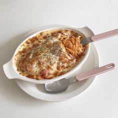 a white plate topped with pasta and cheese covered in sauce next to two spoons