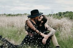 two people are sitting in the grass with their arms around each other and one is kissing