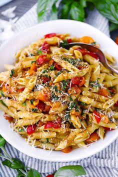 a bowl filled with pasta and vegetables on top of a striped table cloth next to basil leaves