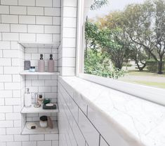 a bathroom with white tile and shelves filled with personal care items next to a window