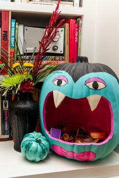 a decorated pumpkin sitting on top of a table next to a vase and bookshelf