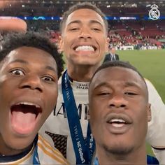 three men standing next to each other in front of a soccer field with their mouths open