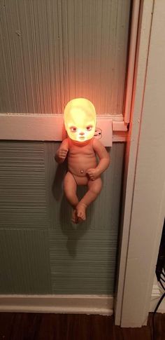 a baby doll with a glowing light on it's head hanging from a door