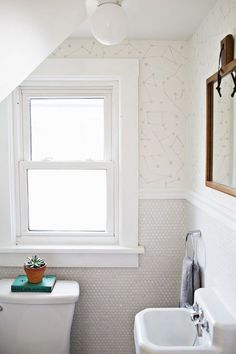 a white toilet sitting next to a sink under a window in a bathroom with wall paper on the walls