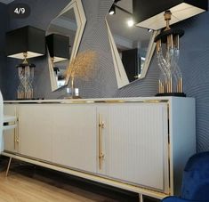 a white and gold sideboard with three mirrors on it's sides, in front of a blue chair