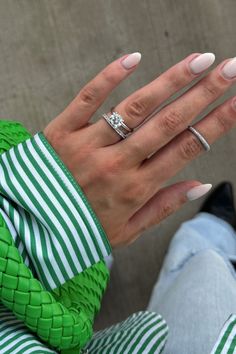 a woman's hand with two rings on top of her fingers, sitting next to a wall