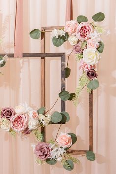 an arrangement of flowers and greenery in front of a pink backdrop