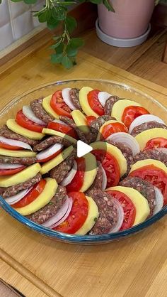 a glass platter filled with sliced tomatoes and hamburger patties on top of a wooden cutting board