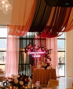 a table with flowers and candles on it in front of a window that has pink drapes