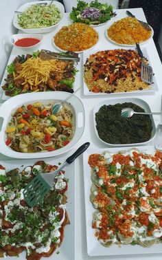 a table filled with lots of different types of food on white plates and serving utensils