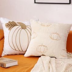 two decorative pumpkin pillows on an orange couch next to a white lace throw pillow and a book