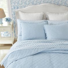 a bed with blue and white comforters in a bedroom next to a lamp on a nightstand