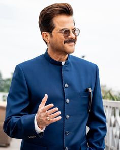 a man in a blue suit and glasses talking to someone with his hand out for the camera