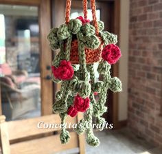 a crocheted hanging decoration with red flowers on the outside of a door way