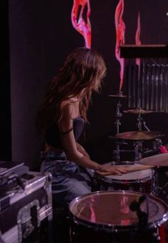 a woman sitting in front of a drum set on top of a wooden floor next to a red light