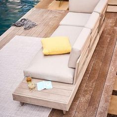 a couch sitting on top of a wooden floor next to a swimming pool with a yellow pillow