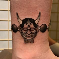 a tattoo on the ankle of a person with two skulls and horns in front of them