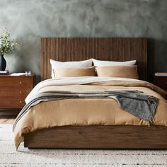 a large bed sitting next to a wooden dresser with drawers on each side and a plant in the corner