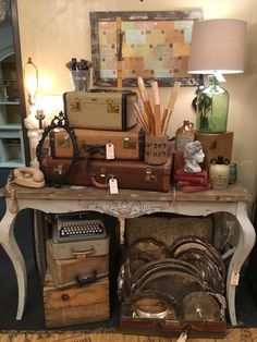 an old table with many pieces of luggage and other items on it in front of a lamp