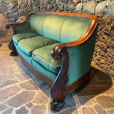 a green couch sitting on top of a stone floor next to a wall with a wooden frame