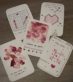 four handprinted cards with hearts and flowers are on a wooden table, next to a calculator