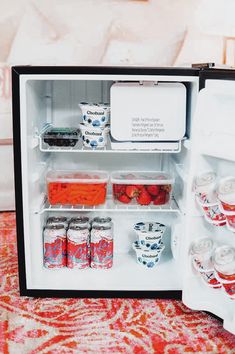 an open refrigerator filled with lots of food on top of a colorful carpeted floor