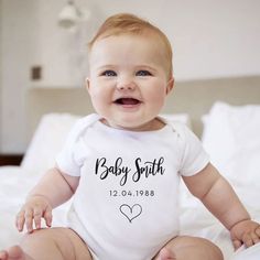 a baby sitting on top of a bed wearing a white shirt with the words baby smith