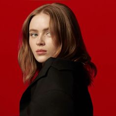 a woman with long hair is standing in front of a red wall and looking at the camera