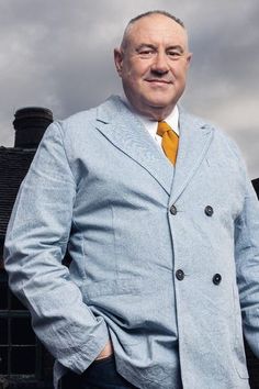 a man in a blue suit and yellow tie posing for the camera with his hands on his hips