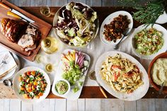 an overhead view of food and wine on a wooden table with utensils, plates, glasses and knives