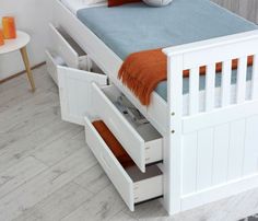 a white bed with drawers underneath it in a room next to a table and chair