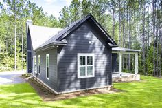 a small gray house in the middle of a forest with trees and grass around it