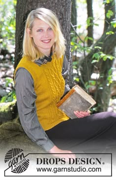 a woman sitting on the ground holding a book in front of a tree and smiling