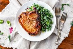 a white plate topped with meat and greens next to a fork, knife and napkin