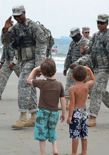 a group of soldiers walking on top of a sandy beach next to the ocean with children