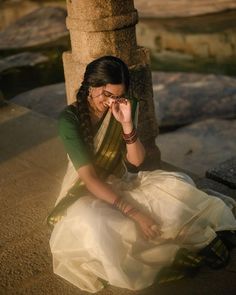 a woman sitting on the ground next to a stone pillar with her hand in her face