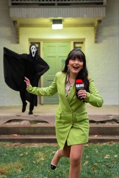 a woman in a green suit is holding a microphone and standing next to a black ghost