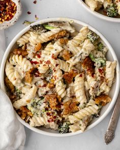 two bowls filled with pasta and broccoli on top of a white countertop