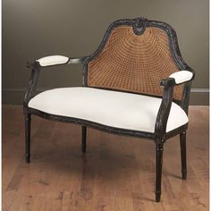 an old fashioned chair with white cushions and caned back rests on a hard wood floor