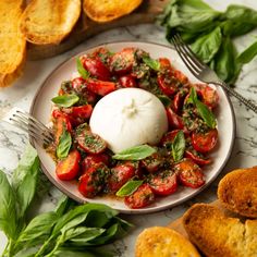 a white plate topped with tomatoes and basil next to garlic bread on a marble table