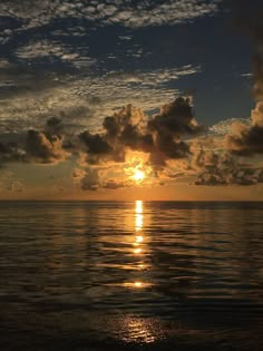 the sun is setting over the ocean with clouds in the sky and water below it