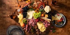 a table topped with lots of different types of cheeses and fruit on top of a wooden floor