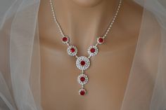 a woman wearing a necklace with red stones and white pearls on the neck, in front of a mannequin