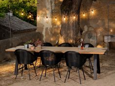 a wooden table with black chairs and lights strung from the tree in front of it